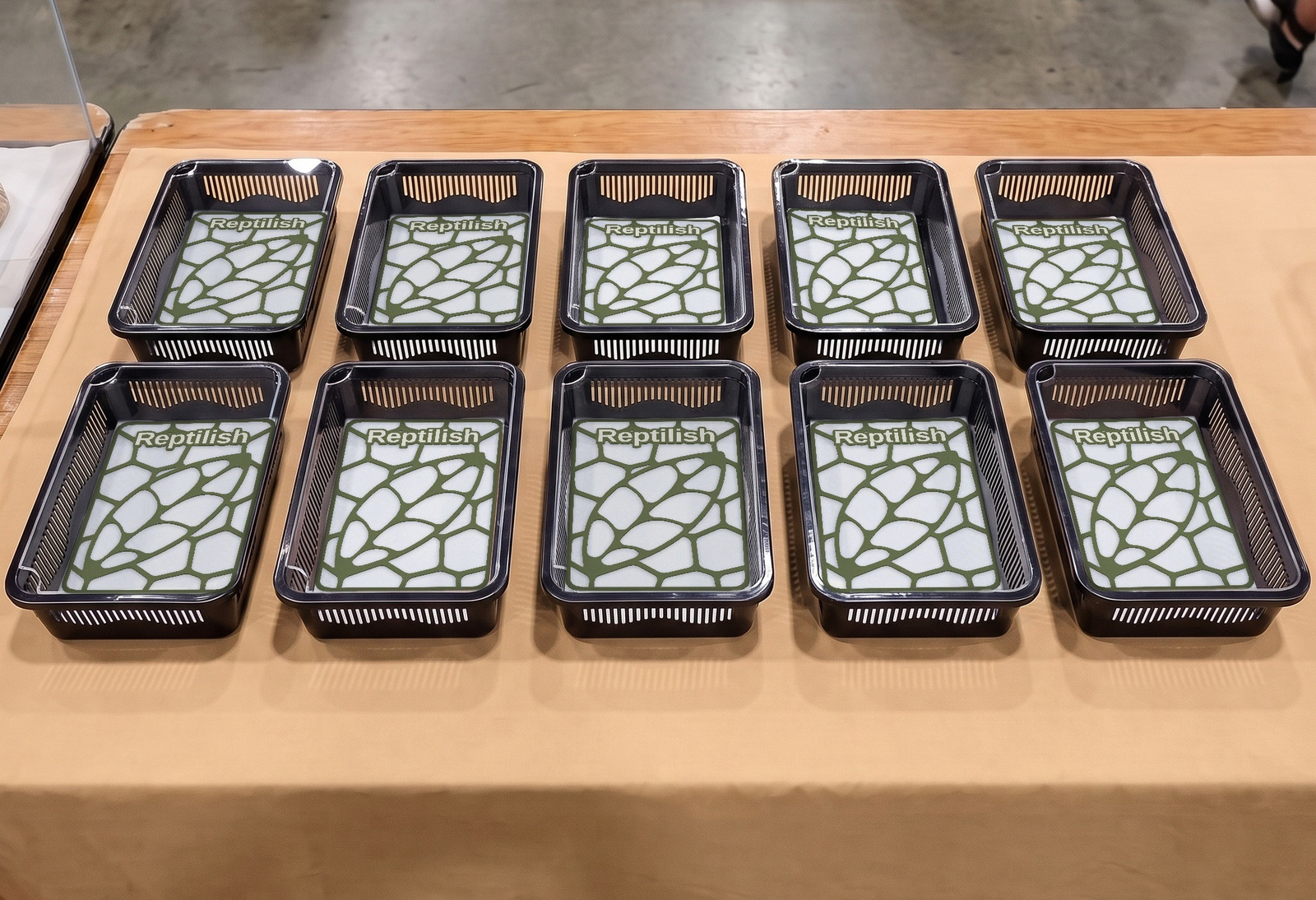 Dieci faunabox neri in due file su un tavolo espositivo in fiera, con dentro piastre Pebble Plate in Verde notte