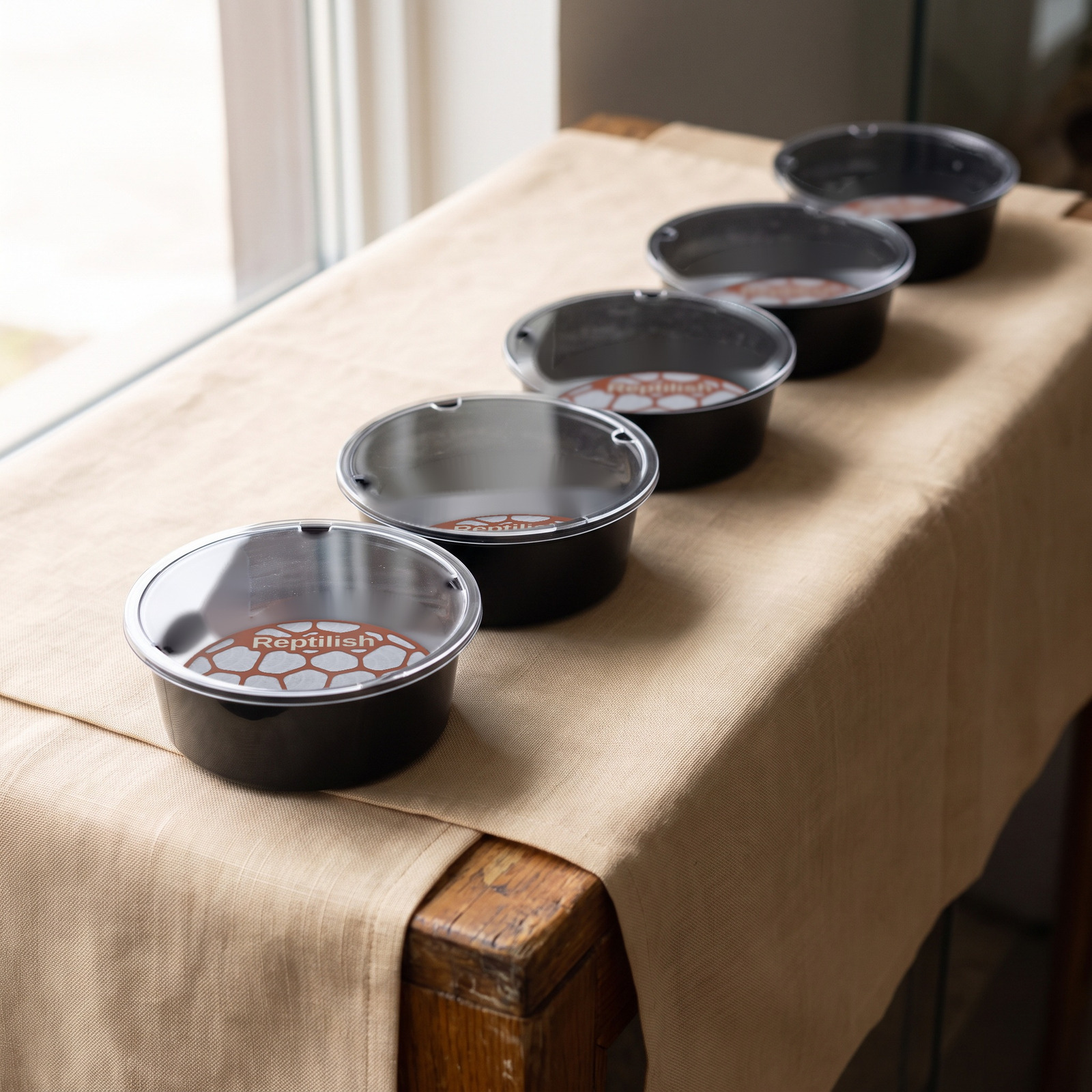 Contenitori tondi con coperchio in acrilico sul bancone di un negozio, con davanti piastre Pebble Plate in Terracotta